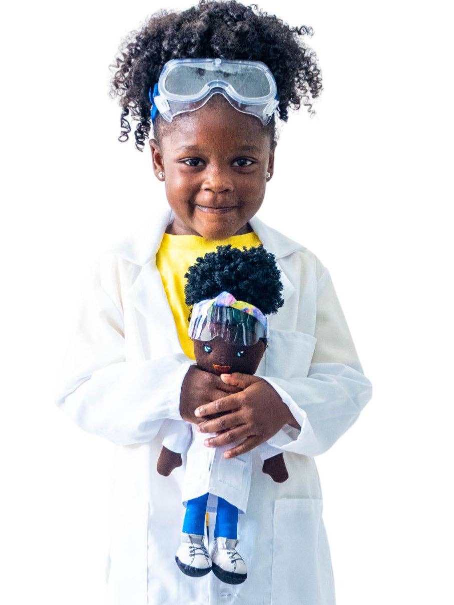 Child in a lab coat holding a doll with a diverse representation, wearing goggles on a white background