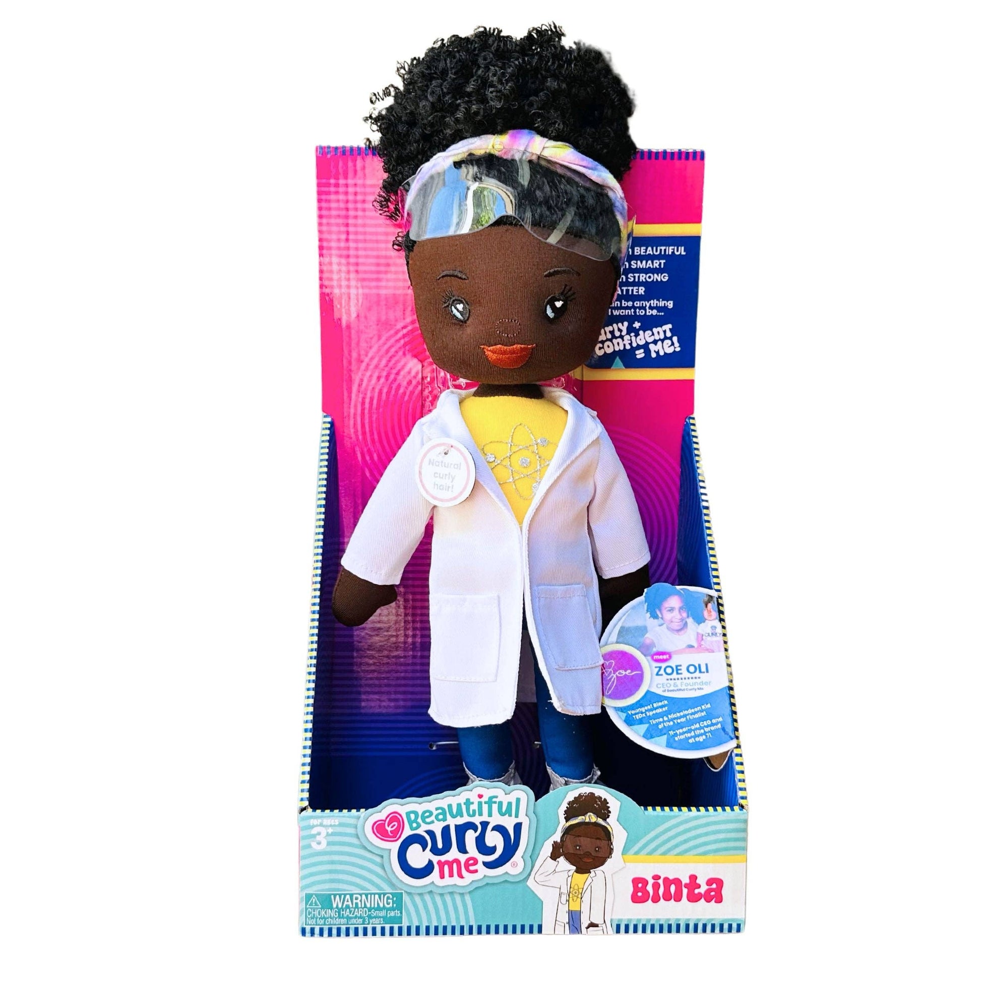 Toy doll with curly hair in a white lab coat, standing in front of its packaging.
