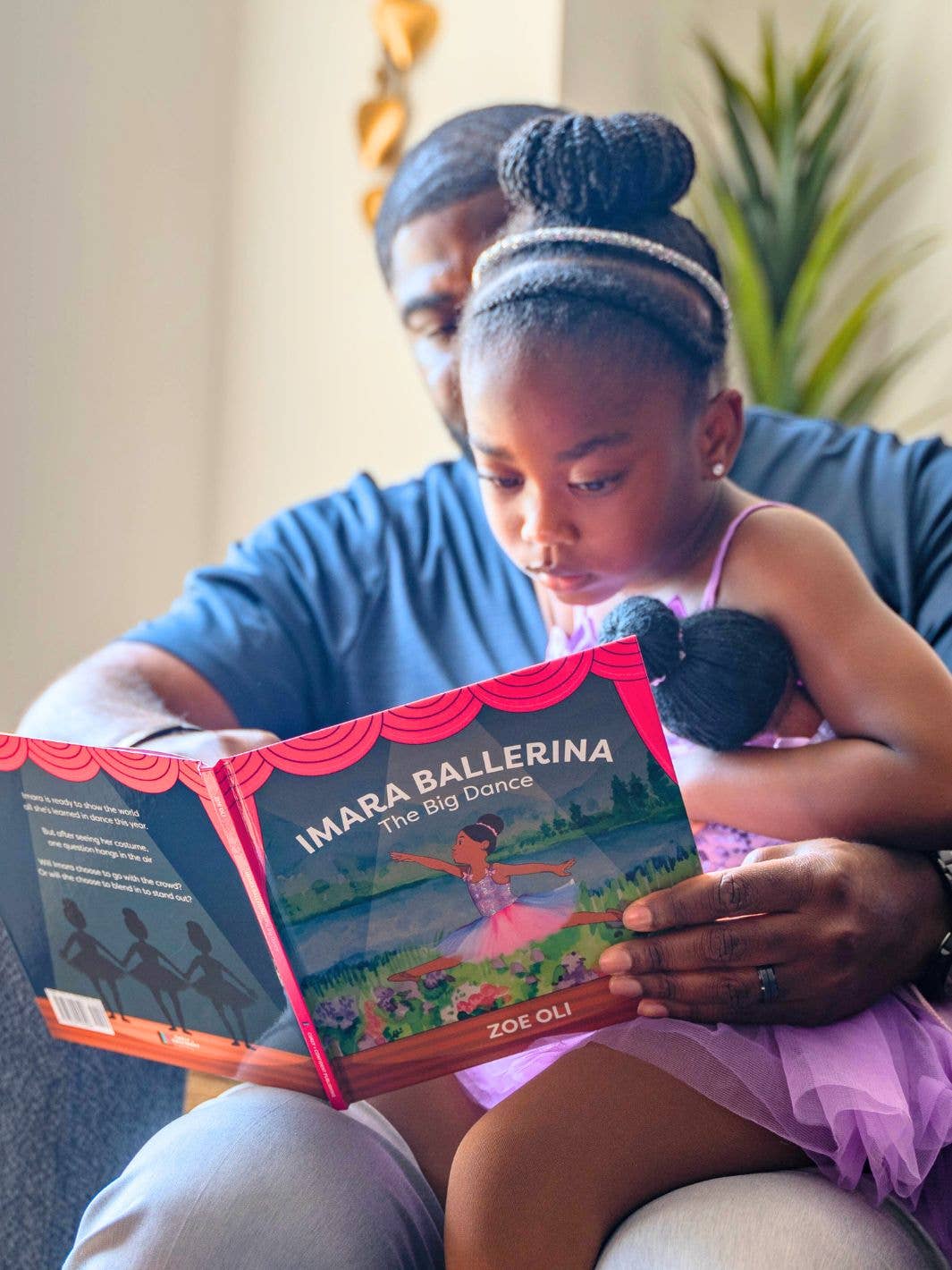 Man and young girl reading a book together, with a focus on the book titled 'Imara Ballerina: The Big Dance' by Zoe Oli.